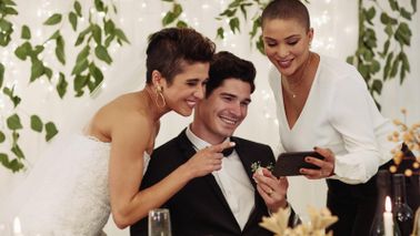 Couple at their wedding with their wedding planner looking at photos on phone