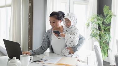 mom working from home while holding toddler in pajamas