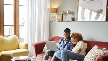 Young couple on a couch looking at a computer and researching mortgage points.
