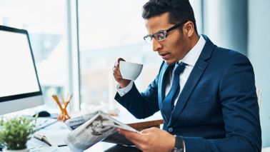 Man at desk drinking coffee and reading Northwestern Mutual Market Commentary.